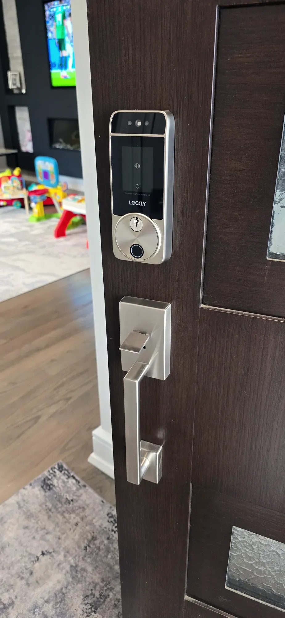 Smart lock with camera and fingerprint reader above a satin handleset on a dark wood entry door